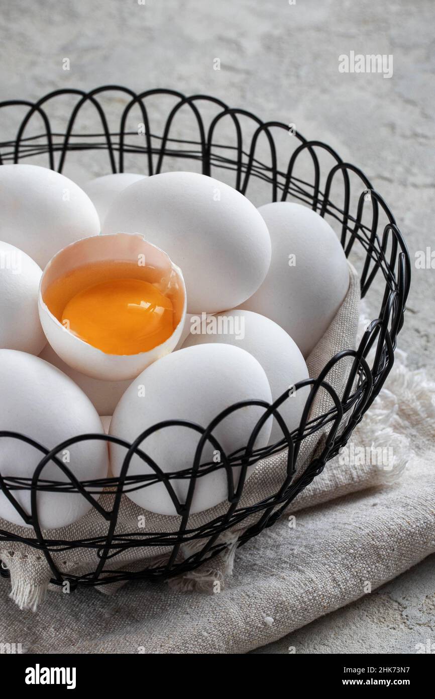 Weiße, große Eier und ein zerbrochenes Ei mit Eigelb in einem eisernen Korb Stockfoto