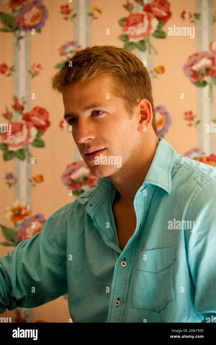 Junger Mann sitzt vor einer Wand mit Blumenmuster Stockfoto