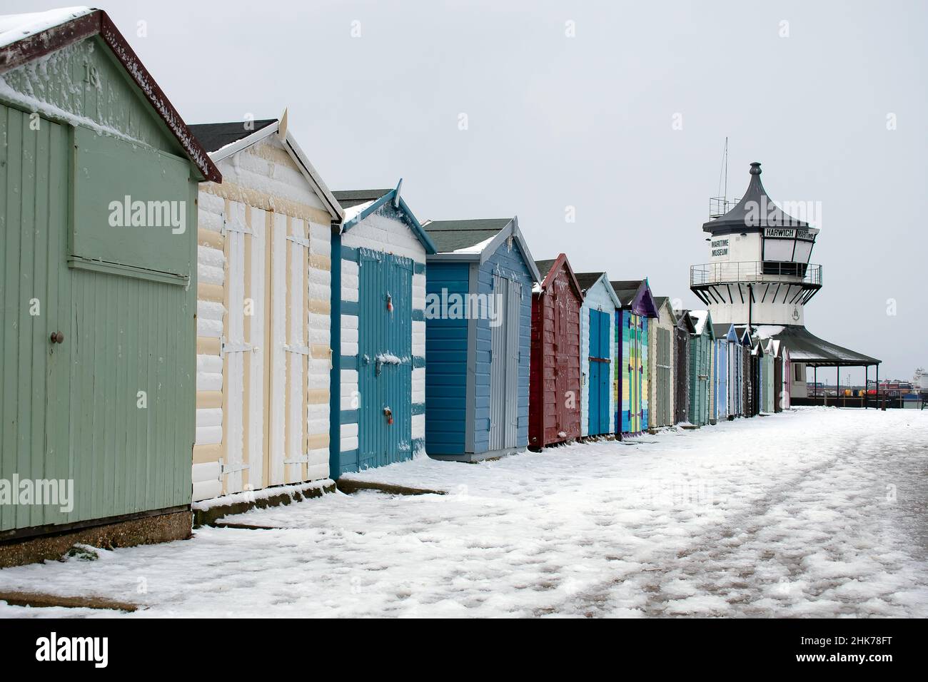 Strandhütten säumen die schneebedeckte Promenade, die zum Harwich Low Lighthouse und Maritime Museum entlang der Küste von North Essex, Großbritannien, führt Stockfoto
