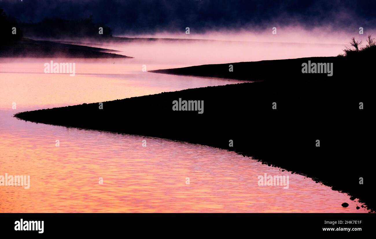 Nebliger Morgen auf dem See mit Dampf, der aus dem Sonnenlicht des Wassers aufsteigt Stockfoto