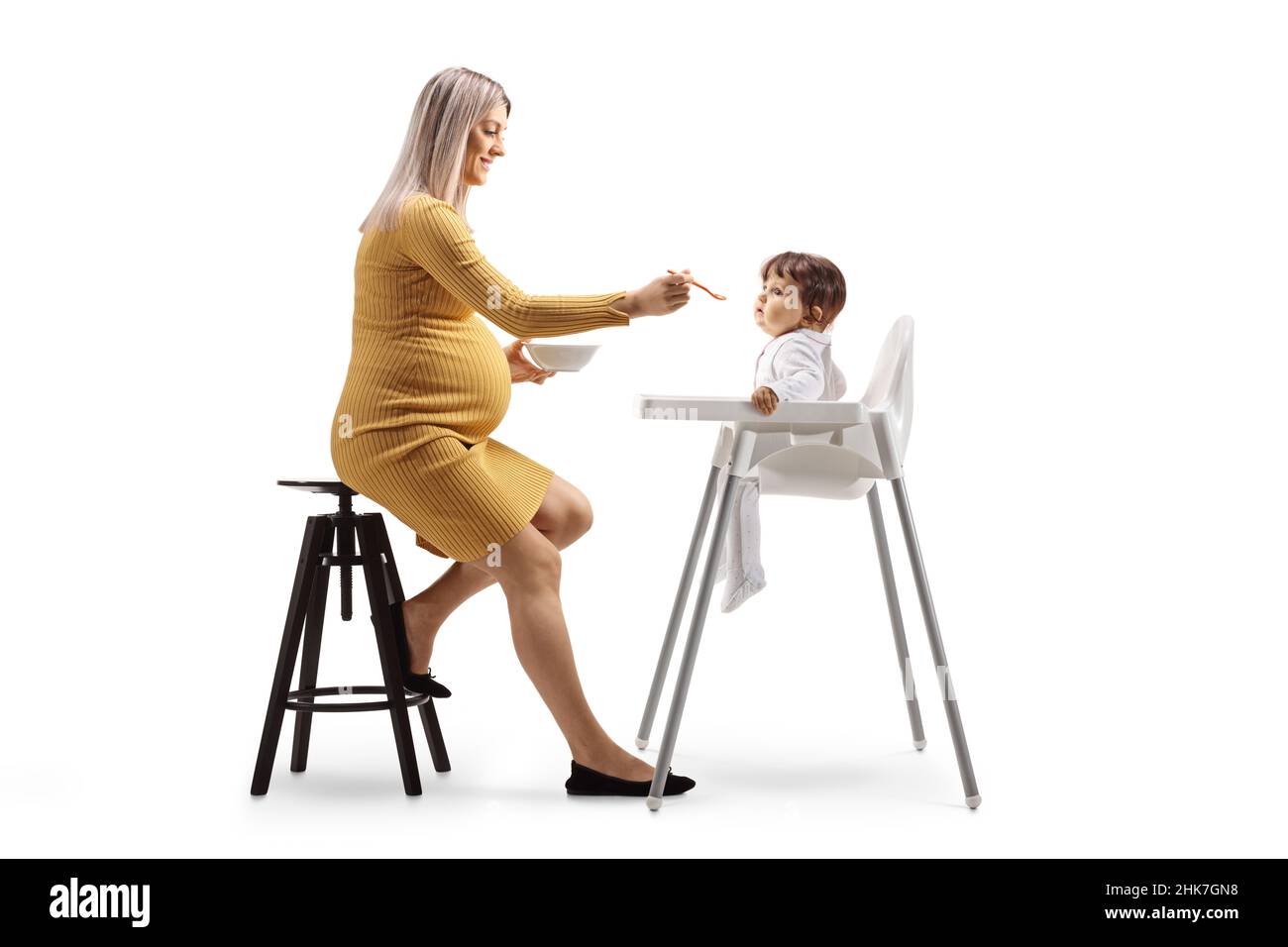 Eine Schwangerin füttert ein Baby auf einem Stuhl, der auf weißem Hintergrund isoliert ist Stockfoto