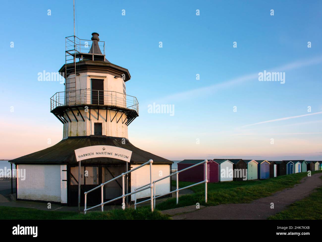 Harwich Low Lighthouse und Harwich Maritime Museum mit farbenfrohen Strandhütten entlang der Nord-Essex-Küste, wenn die Farben des Sonnenuntergangs in den Himmel eintreten. Stockfoto