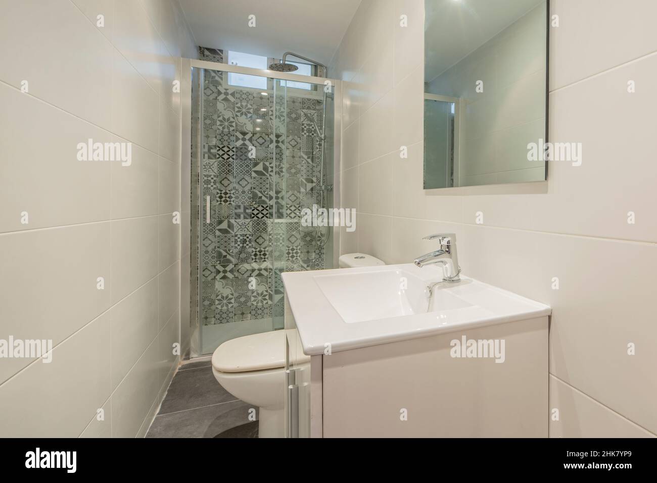 Das Badezimmer ist modern eingerichtet und verfügt über eine Duschwand mit hydraulischen Fliesen, einen weißen Kosmetikbereich und einen rahmenlosen Glasspiegel Stockfoto