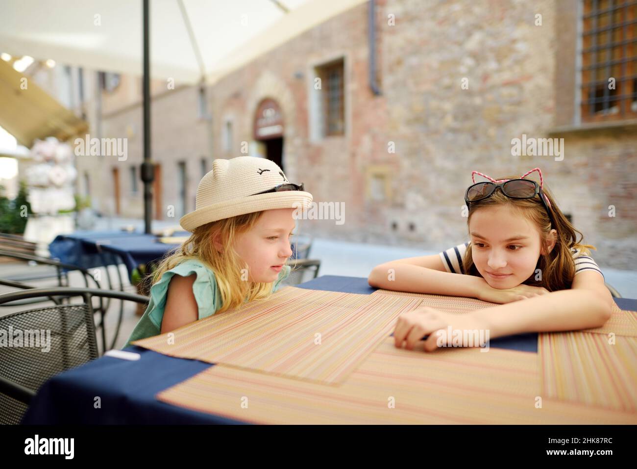 Zwei Schwestern sitzen in der Pizzeria im Freien in der alten engen Straße der berühmten Stadt Montepulciano, die sich auf einem Kalksteinkamm befindet, der von Weinbergen umgeben ist Stockfoto