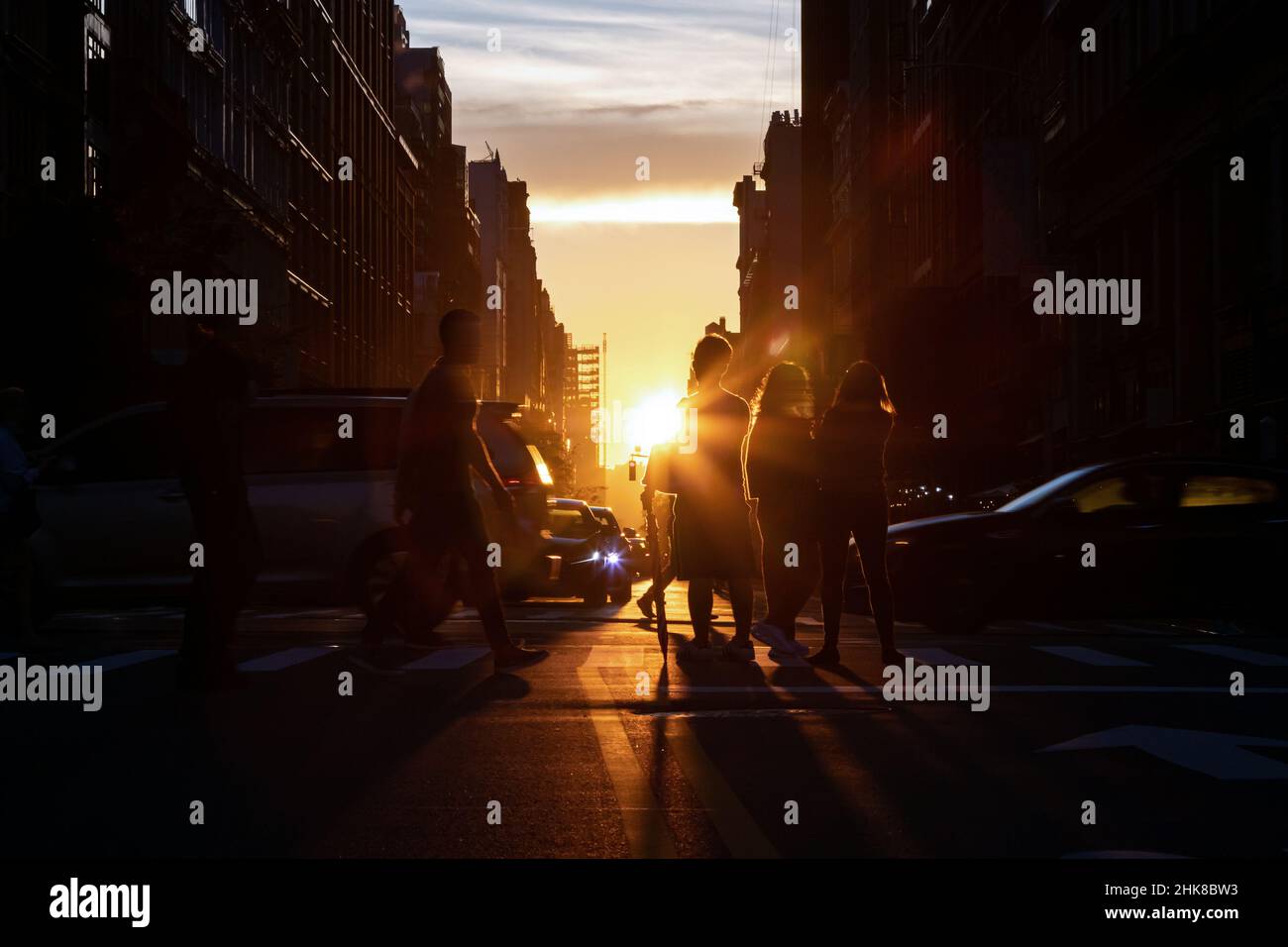 Belebte Straßenszene mit Menschenmassen und Autos an einer Kreuzung auf der 5th Avenue in New York City mit Sonnenlicht leuchtendem Hintergrund Stockfoto