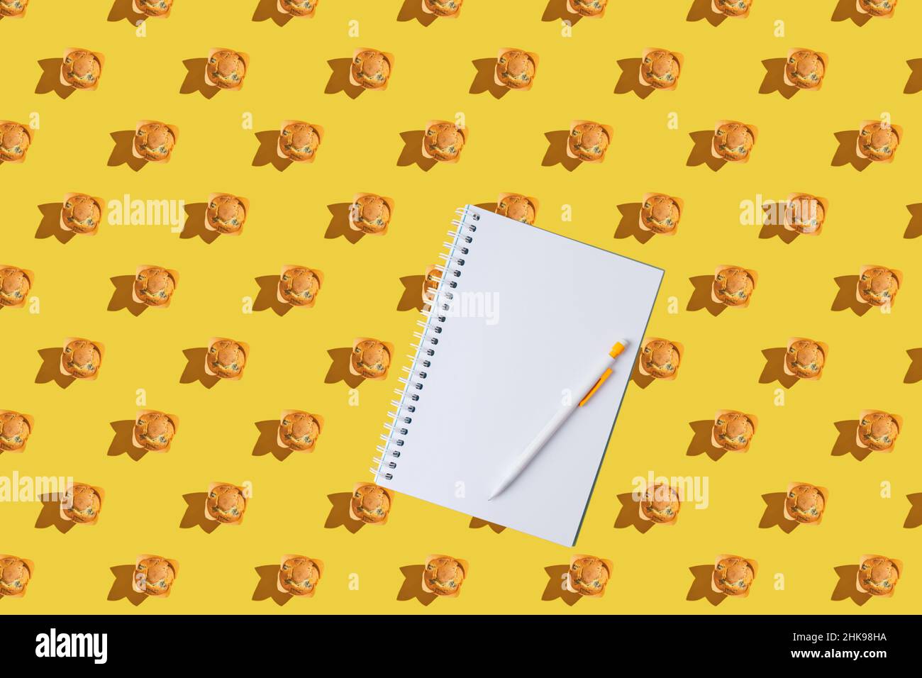 Ein Muster aus Muffins mit Notizblock auf gelbem Hintergrund. Flach liegend. Platz für Text, Platz zum Kopieren. Stockfoto