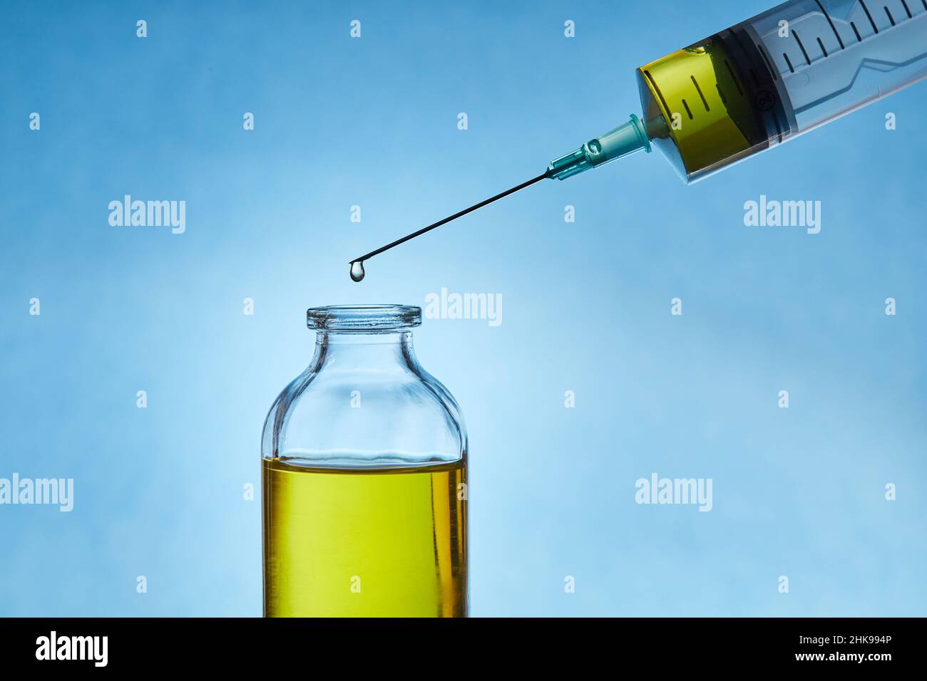 Ein Tropfen Flüssigkeit tropft von der Nadel einer medizinischen Spritze in die Flasche. Vorderansicht. Makrofoto. Stockfoto