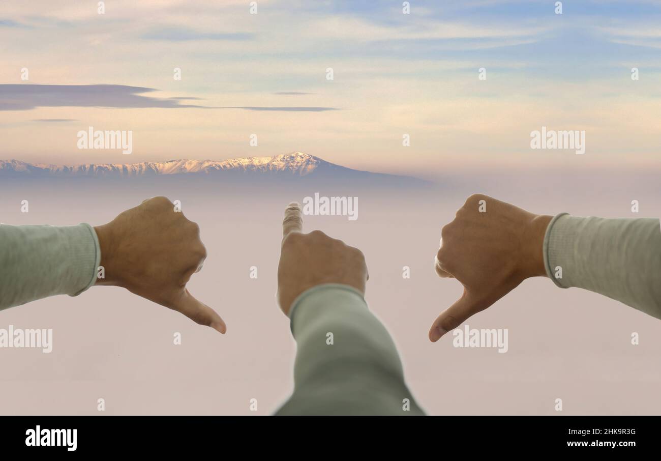Eine Hand zeigt nach oben, andere nach unten auf den Hintergrund des Berggipfes. Konzept des Glaubens, Motivation, Weitsicht, Ziel. Stockfoto