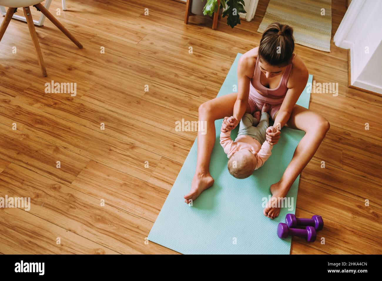 Ansicht von oben einer Mutter, die mit ihrem Baby auf einer Trainingsmatte trainiert. Fürsorgliche Mutter macht zu Hause mit ihrem Baby Sit-up-Übungen. Neue Mutter, die sich mit ihr verklebt Stockfoto