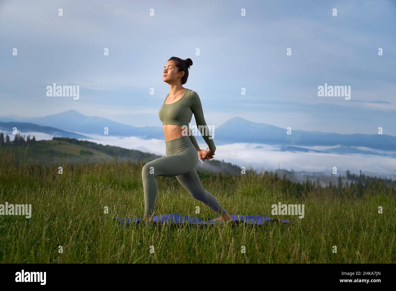 Attraktive Frau tut Stretching zwischen Bergen Natur und tief atmen. Weibchen halten genießen und sich selbst Gleichgewicht in der Praxis von Yoga auf Matte. Konzept der Outdoor-Aktivität. Stockfoto