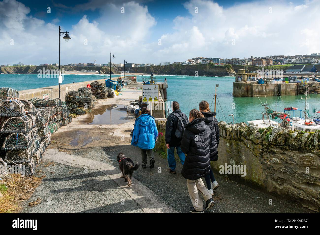 Eine Familie von Urlaubern und ihrem Hund, die zum North Quay im malerischen, funktionierenden Hafen in Newquay in Cornwall wandern. Stockfoto