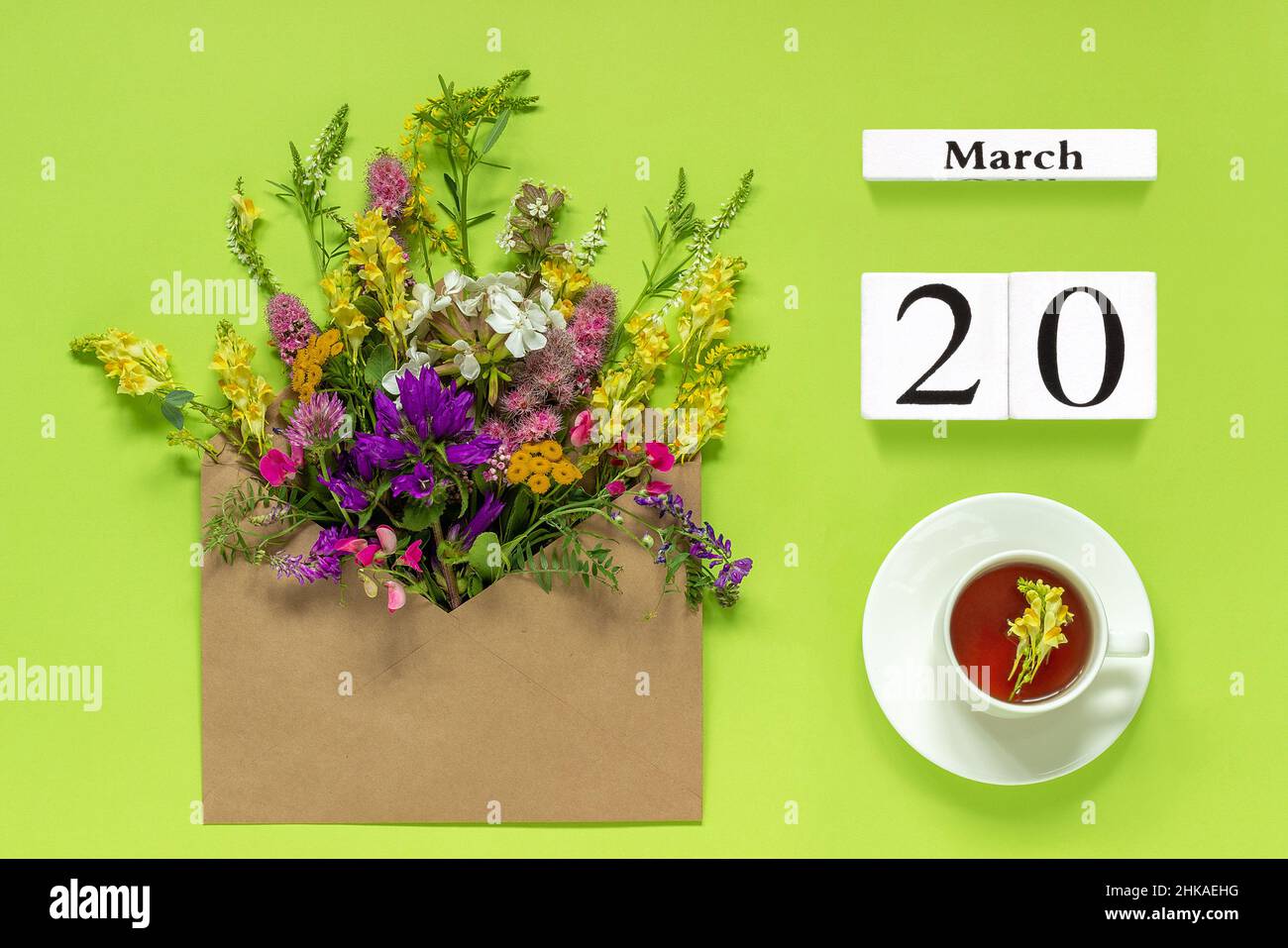 Holzwürfel Kalender März 20. Tasse Kräutertee, Kraftumschlag mit bunten Blumen auf grünem Hintergrund. Konzept Frühling Tagundnachtgleiche Tag Kreativ T Stockfoto