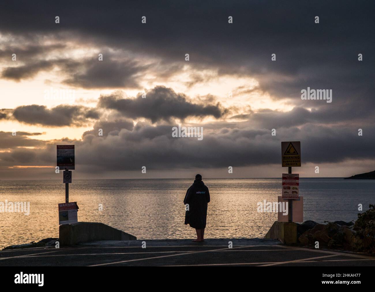 Fountainstown, Cork, Irland. 03rd. Februar 2022. Die Morgenschwimmerin Aoife O'Donovan beobachtet, wie sich ein launischer Himmel entwickelt, während die Dämmerung vom Slipway in Fountainstown, Co. Cork, Irland, bricht. - Credit; David Creedon / Alamy Live News Stockfoto