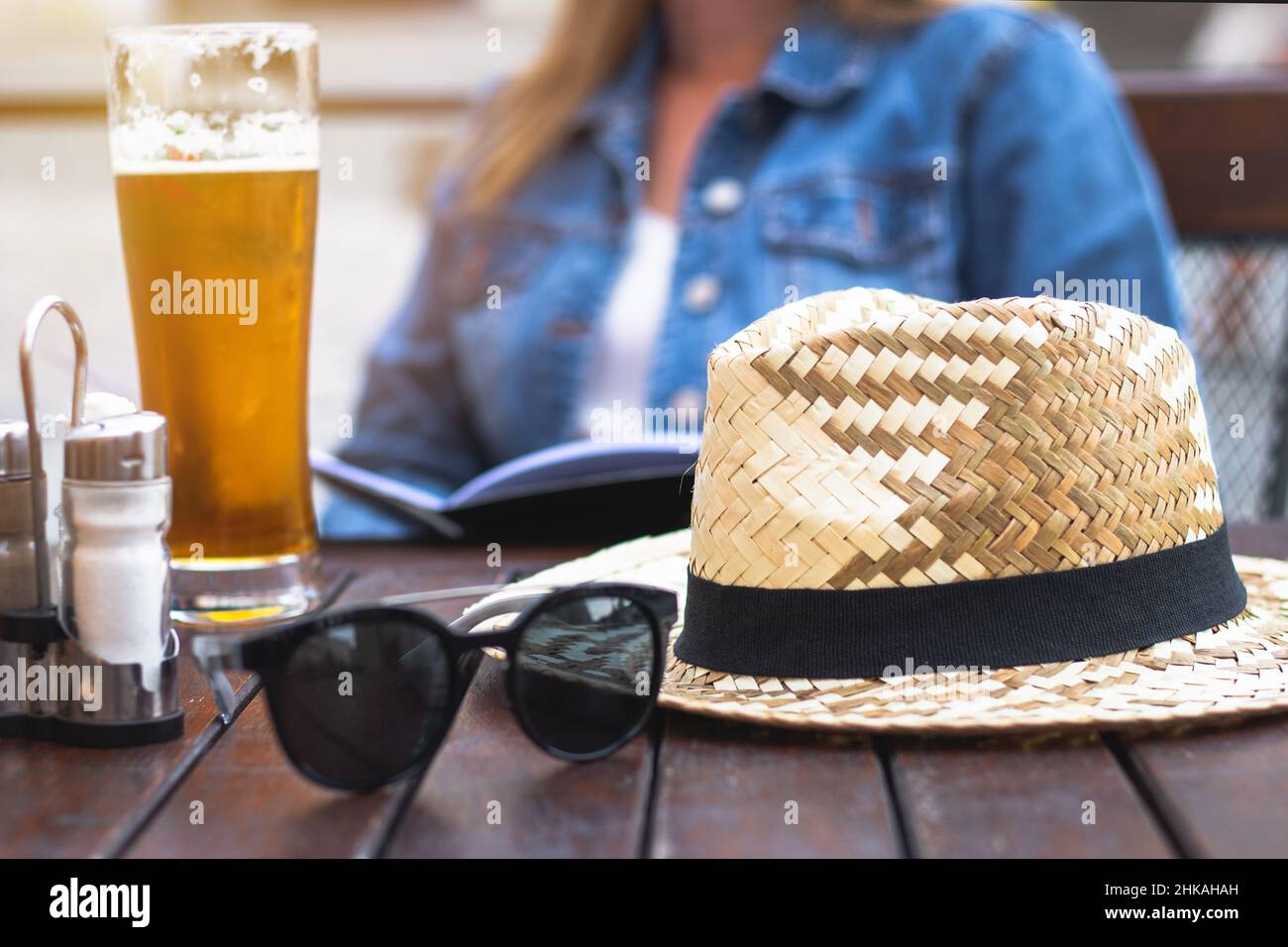 Frau bestellt Essen im Restaurant im Freien. Strohhut und Sonnenbrille auf einem Holztisch. Ein Glas Bier im Pub. Stockfoto