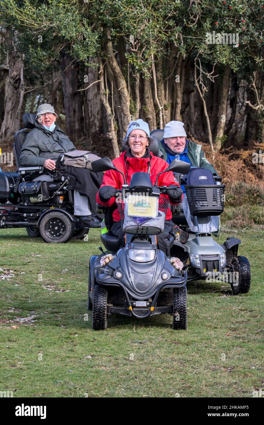 Drei Glückliche Menschen Mit Behinderungen Auf Mobilitäts-Scootern Off Road Auf Dem Land. Teil von Hampshire Roamability, New Forest UK Stockfoto
