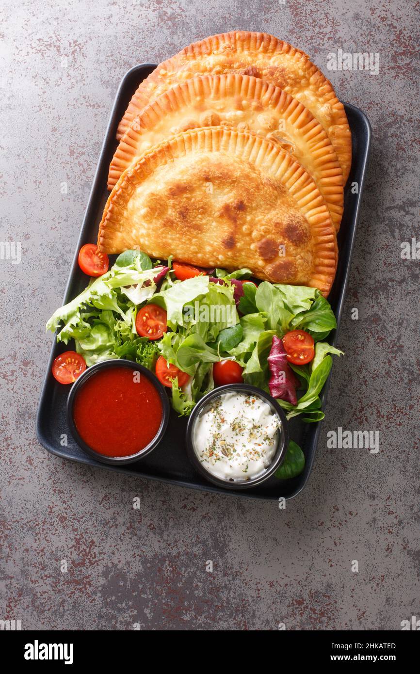 Traditionelle russische frittierte Fleischpasteten Chebureki mit frischem Salat und Saucen in der Nähe auf einem Teller auf dem Tisch. Vertikale Draufsicht von oben Stockfoto