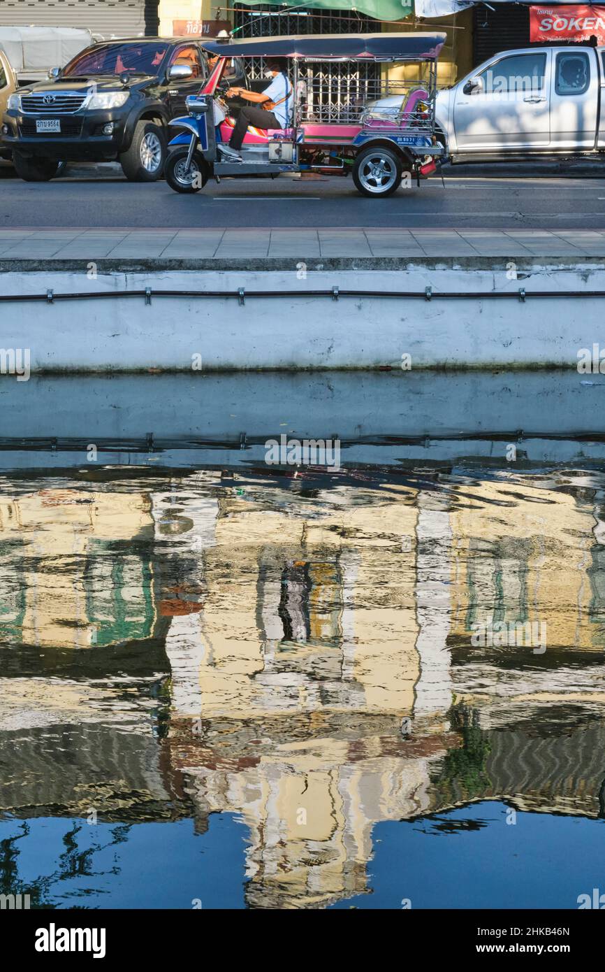 Spiegelungen eines alten Gebäudes im europäischen Stil in Klong (Kanal) Lod neben der Atsadang Rd in Bangkok, Thailand, ein Tuk-Tuk auf der Straße darüber Stockfoto