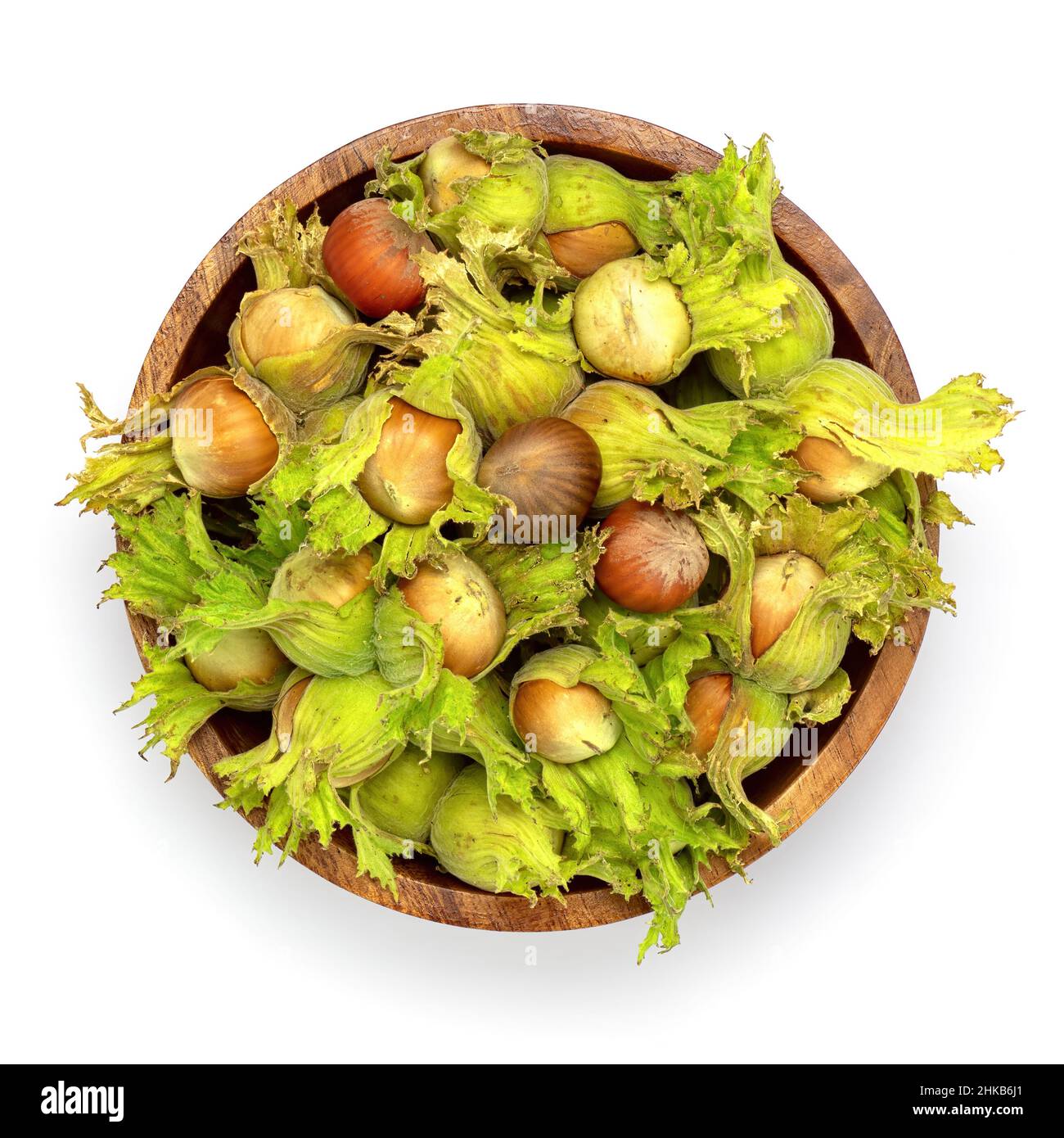 Frische grüne Haselnüsse mit grünen Blättern in Holzschüssel isoliert auf weiß. Stockfoto
