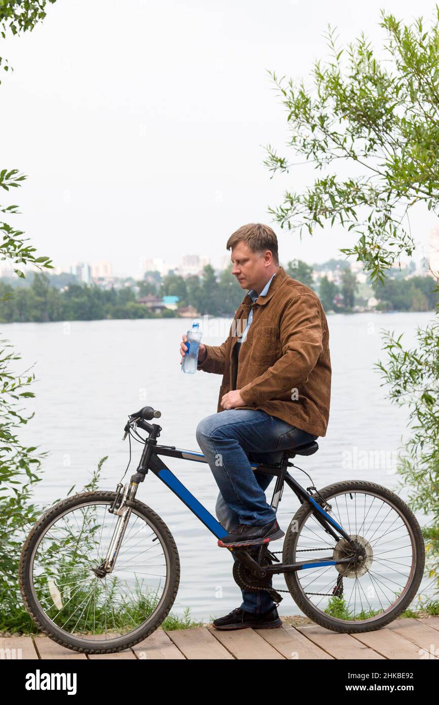 Müde Erwachsene Mann mit einer Flasche Wasser hielt während einer Radtour an, um Wasser zu trinken. Stockfoto