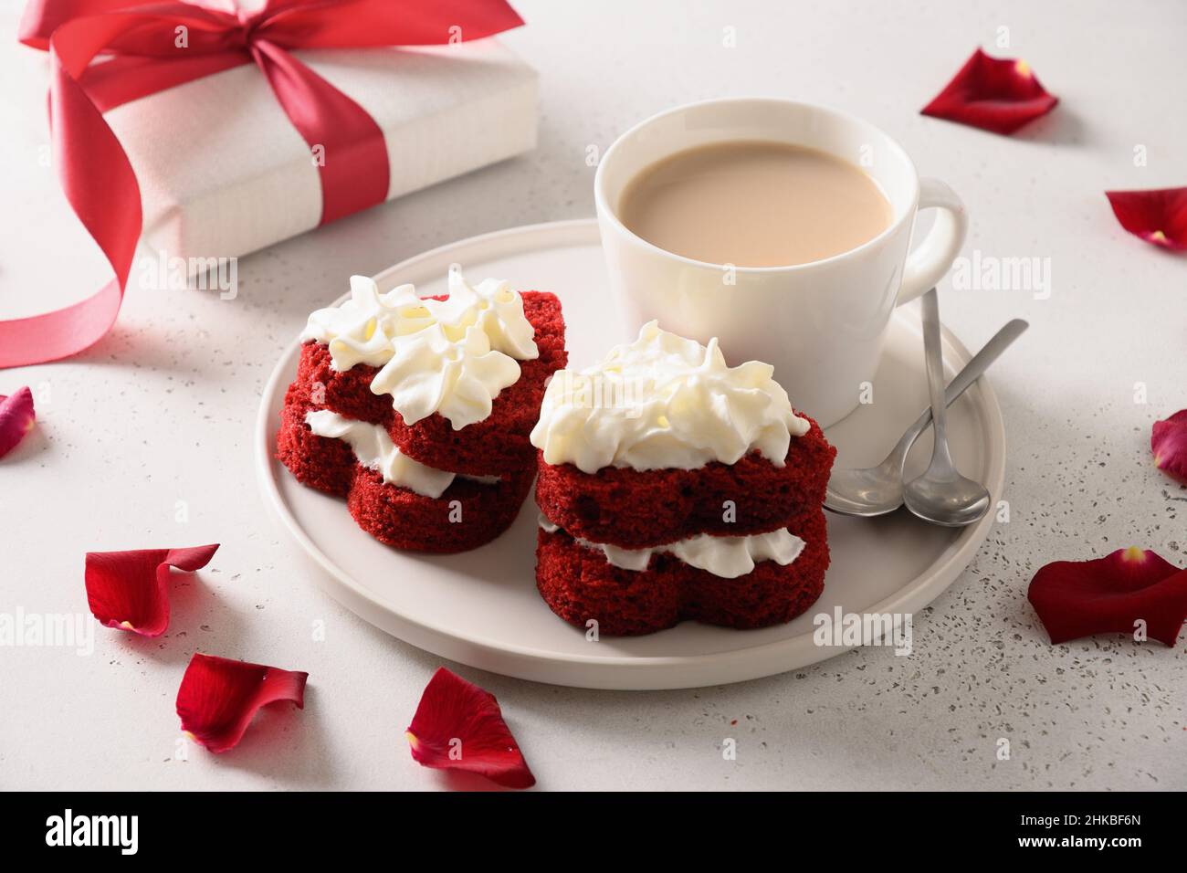 Roter Samtkuchen in Form von Herzen und Kaffee zum Valentinstag auf weißem Hintergrund. Leckeres Dessert. Nahaufnahme. Stockfoto
