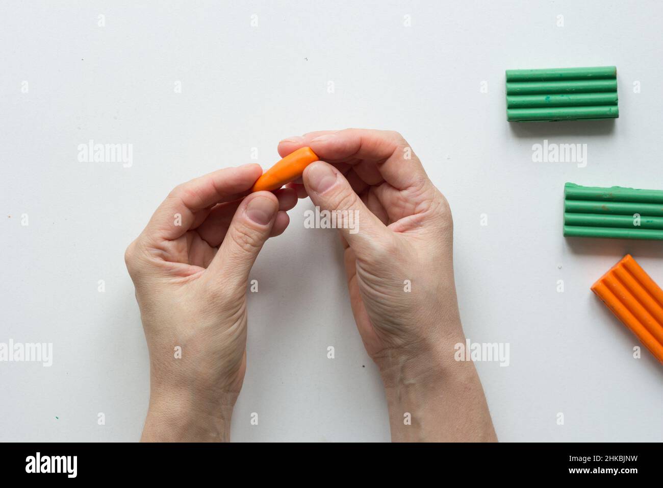 Frau Hände machen kleine Karotten Fimo auf dem weißen Hintergrund Stockfoto