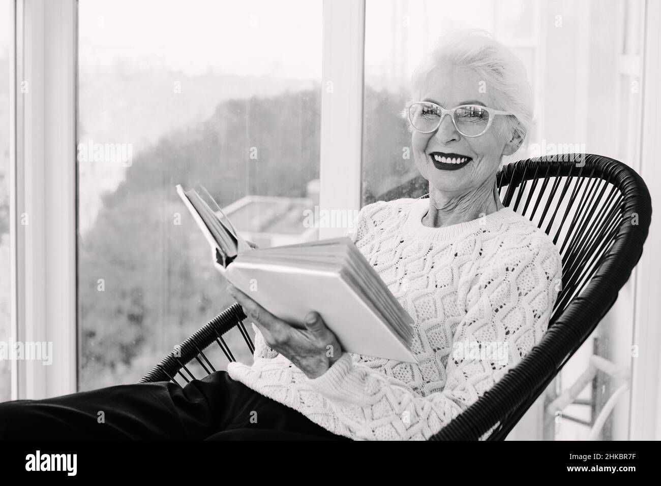 Ältere, stilvolle Frau, die auf der Terrasse sitzt und Buch liest. Bildung, Hobby-Konzept Stockfoto