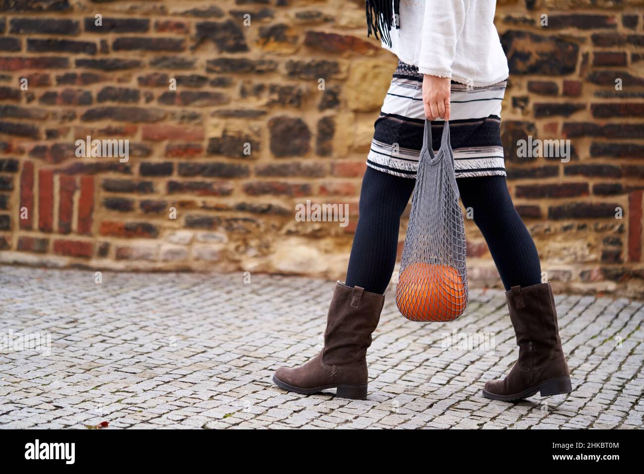 Frau, die im Herbst eine Netztasche mit einem Kürbis im Freien vor einer Wand trägt Stockfoto