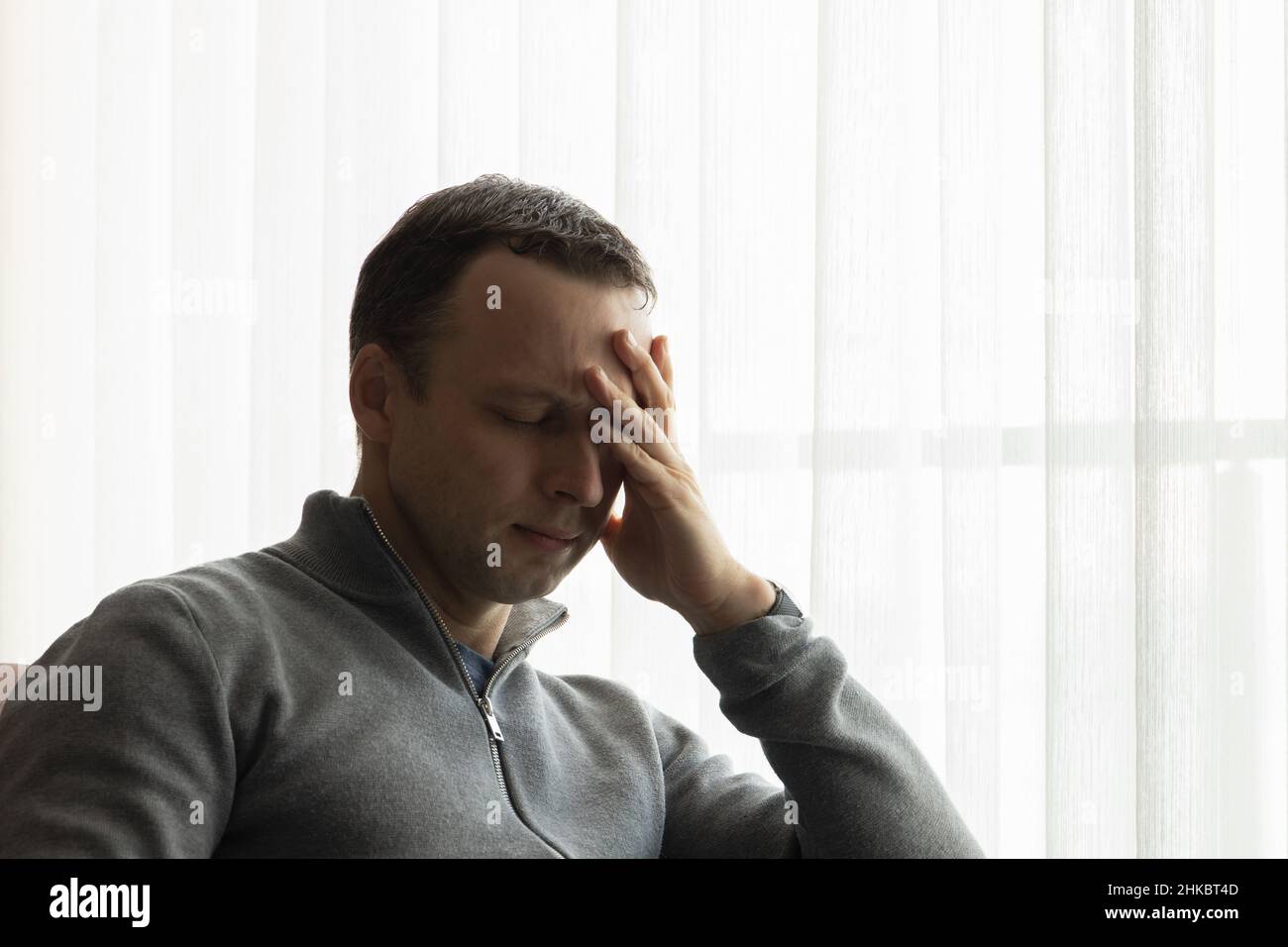 Müder Mann mit geschlossenen Augen sitzt neben einem Fenster, zwangloses Studiofoto Stockfoto
