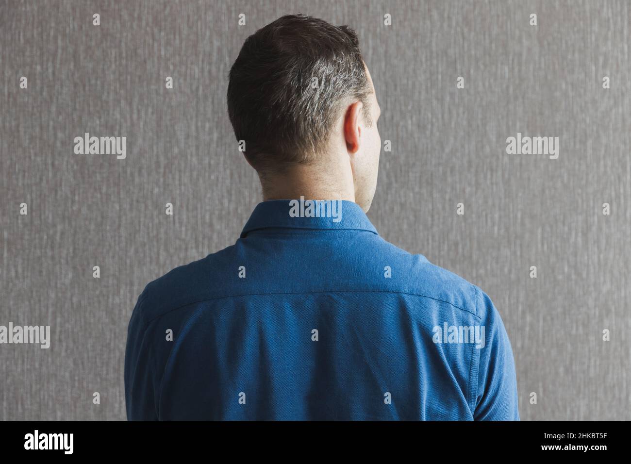 Rückseite eines jungen erwachsenen europäischen Mannes in blauem Hemd, der vor einer grauen leeren Wand steht, legeres Studiofoto Stockfoto