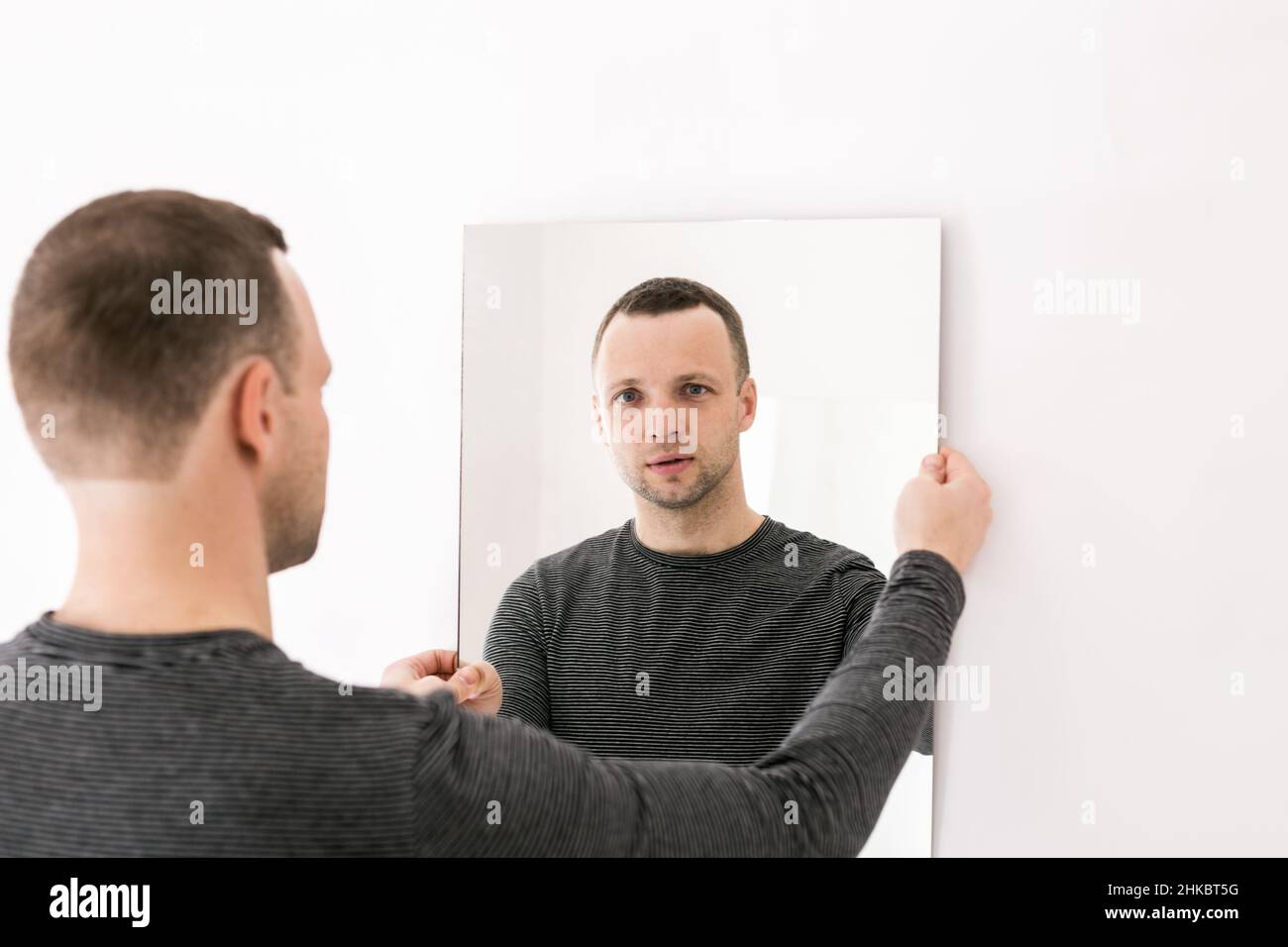 Studioporträt eines jungen Mannes, der vor einer weißen Wand mit einem Spiegel in den Händen steht Stockfoto