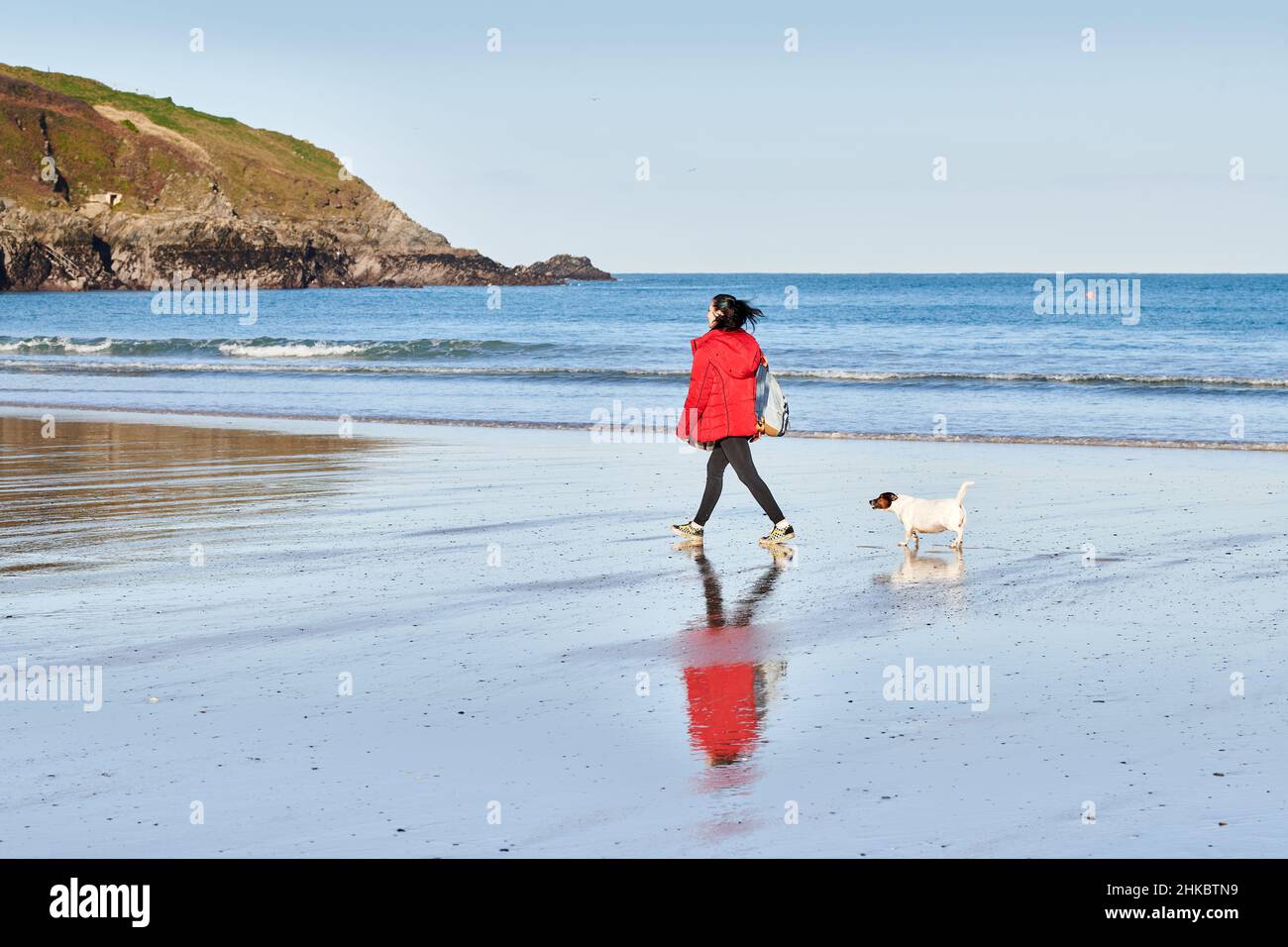 Eine Frau schreitet mit ihrem Hund am Towan Beach, Newquay, Cornwall, England, entlang der Küste. Stockfoto