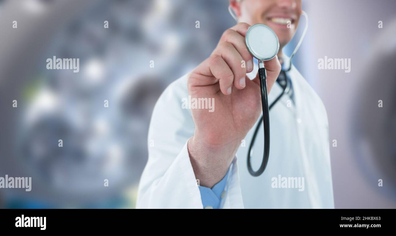 Mittelteil eines lächelnden kaukasischen männlichen Arztes mit mittlerem Erwachsenen, der Stethoskop hielt, während er im Krankenhaus stand Stockfoto