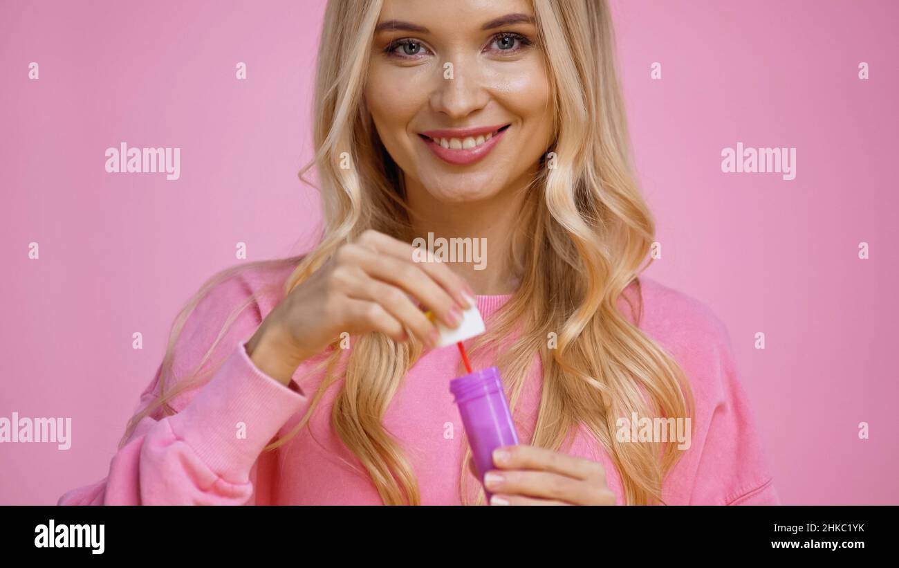 Fröhliche blonde Frau hält Zauberstab und Seifenblasen isoliert auf rosa Stockfoto