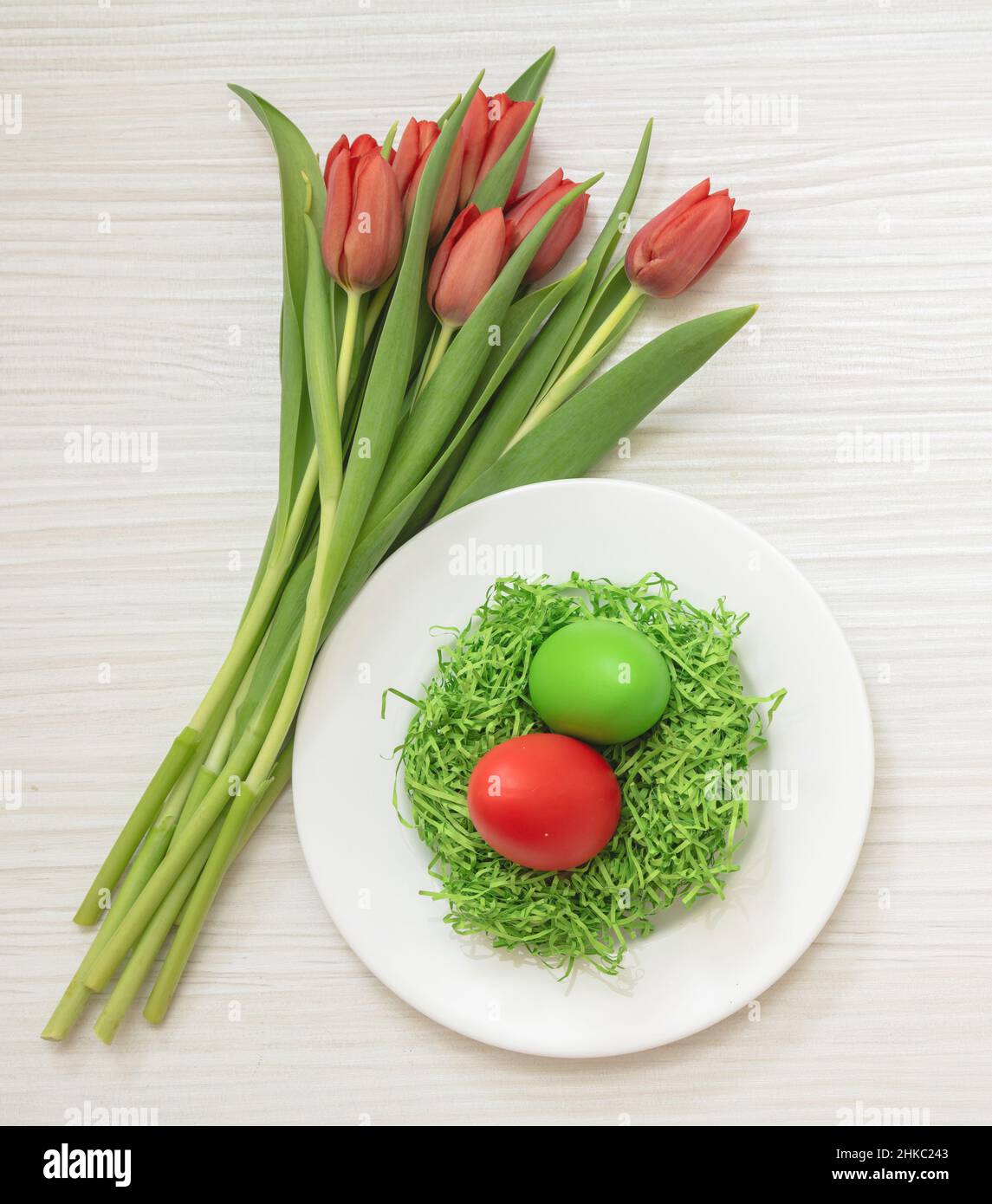 Ostern Tischfeier. Eiernest und rote Tulpen Dekoration auf weißem Holzhintergrund, Draufsicht, Frühlingsferien Stockfoto