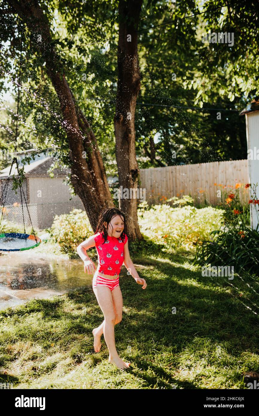 Im Sommer läuft das junge Mädchen durch den Sprinkler im Hinterhof Stockfoto