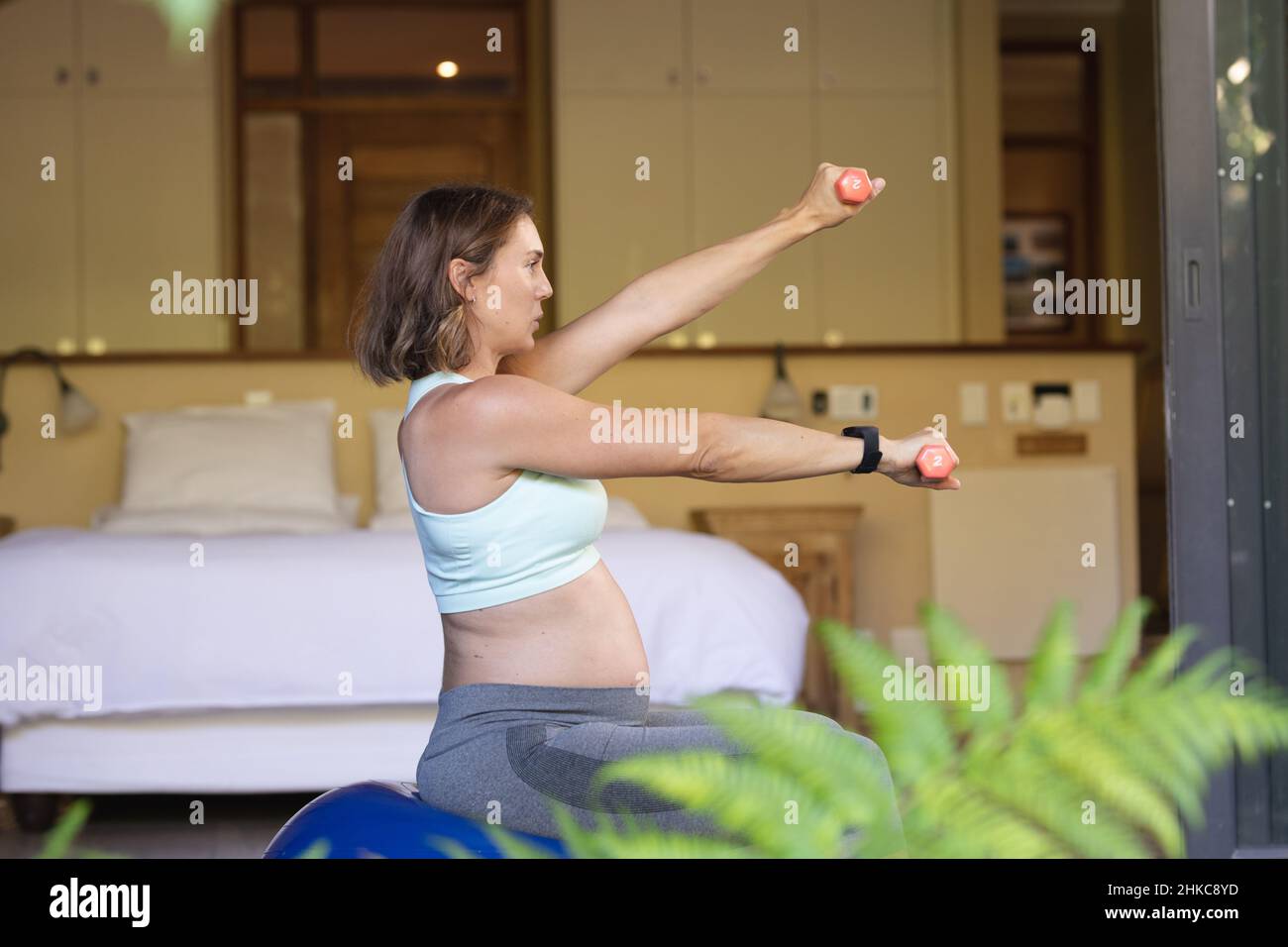 Kaukasische Schwangerin, die zu Hause mit Hanteln auf dem Übungsball trainiert Stockfoto