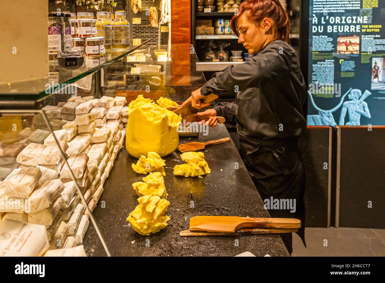 Eine Verkäuferin im Maison du Beurre Bordier in Saint-Malo, Bretagne, Frankreich, schneidet mit zwei hölzernen Schaufeln kleine Portionen von einem großen Butterblock ab. Jede fertige Portion wiegt 125 Gramm, das Standardformat des Ladens in Handform. Die Fassade des Ladens nennt 1927 als Gründungsjahr; das heutige Beurre Bordier-Geschäft geht zurück auf Jean-Yves Bordier, der hier 1984 die traditionelle Handschlagmethode seines Großvaters wiederbelebte. Stockfoto