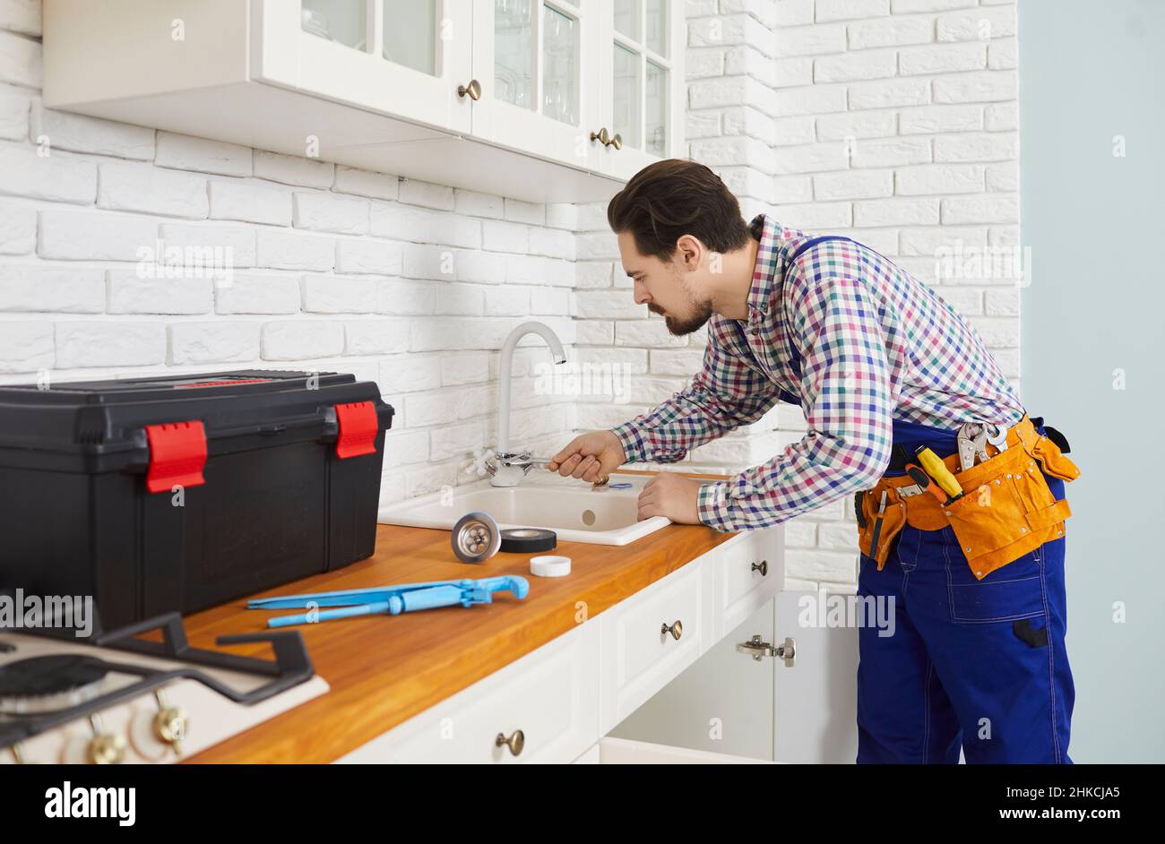 Professioneller Klempner installiert oder repariert Wasserhahn und Waschbecken in der Küche der Wohnung. Stockfoto