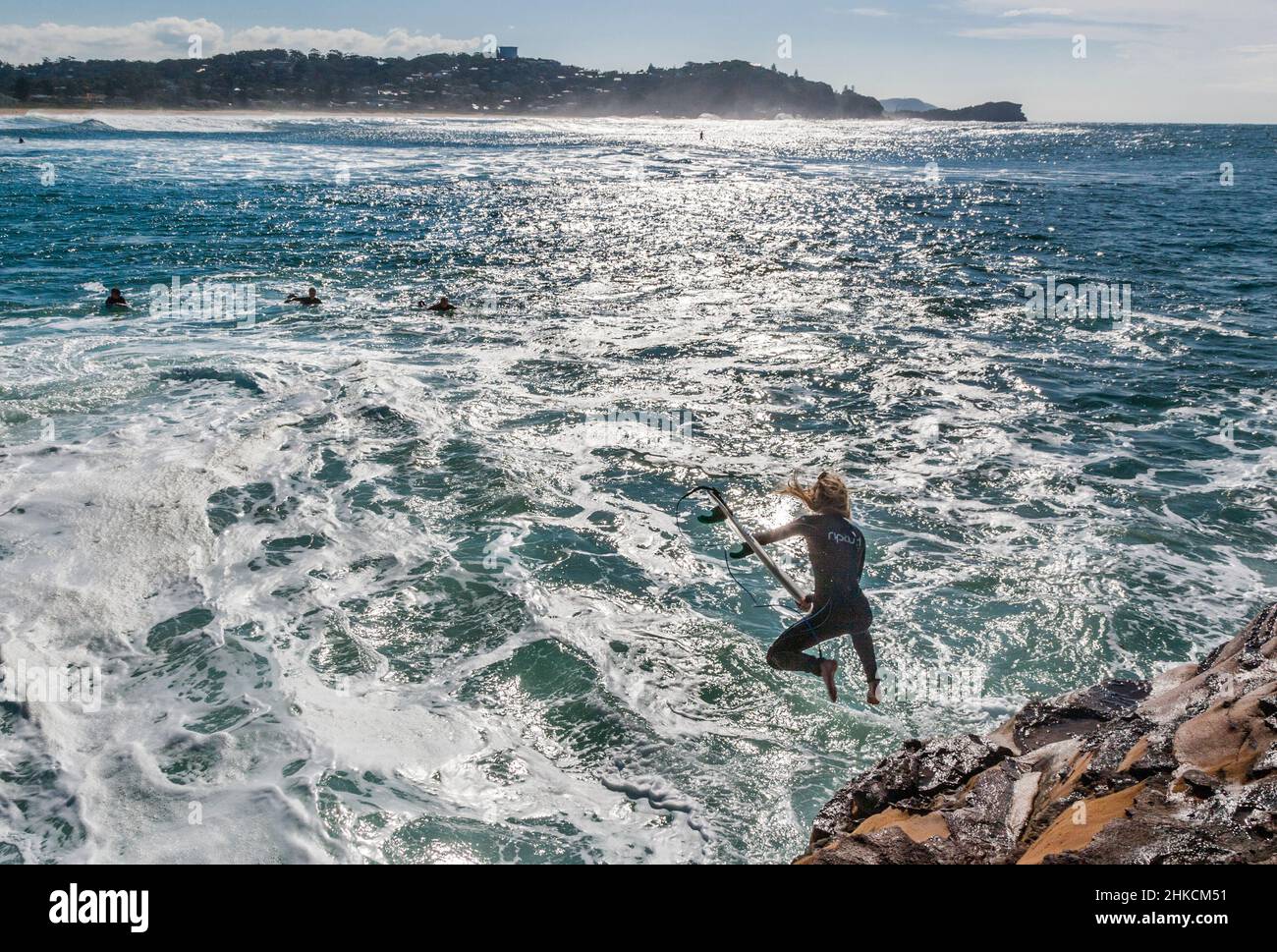 Surfer springen von der gefährlichen Küstenfelsplattform in Mugs Rock, Avoca Beach, Central Coast, New South Wales, Australien in die turbulente Brandung Stockfoto