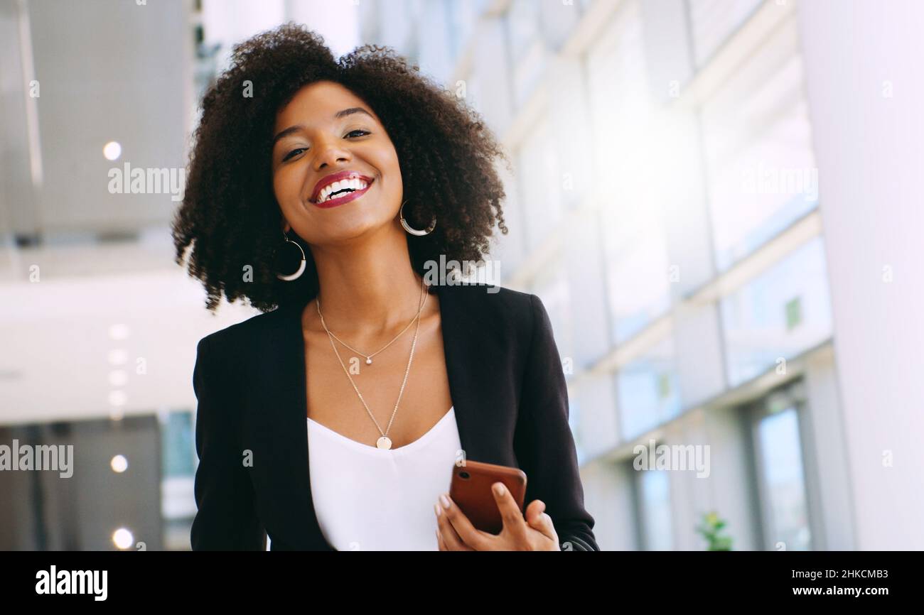Es ist wie mein eigener tragbarer persönlicher Assistent. Aufnahme einer jungen Geschäftsfrau, die ein Smartphone benutzt, während sie durch ein modernes Büro geht. Stockfoto