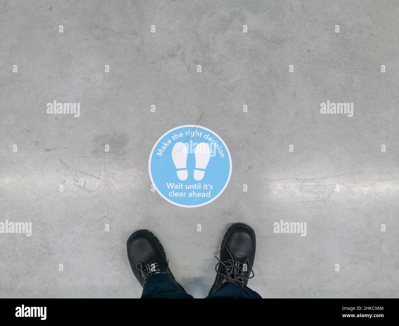 Schilder, die darauf hinweisen, dass der Abstand auf dem Boden eines Lagerhauses mit Sicherheitsschuhen vor ihm zu sehen ist. Stockfoto