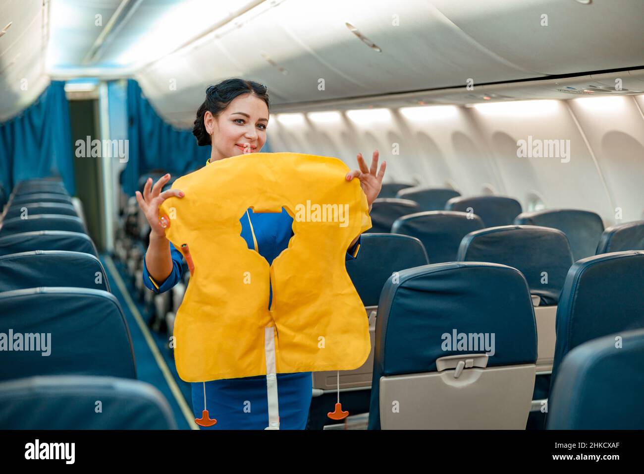 Weibliche Flugbegleiterin mit Schwimmweste im Flugzeug stehend Stockfoto