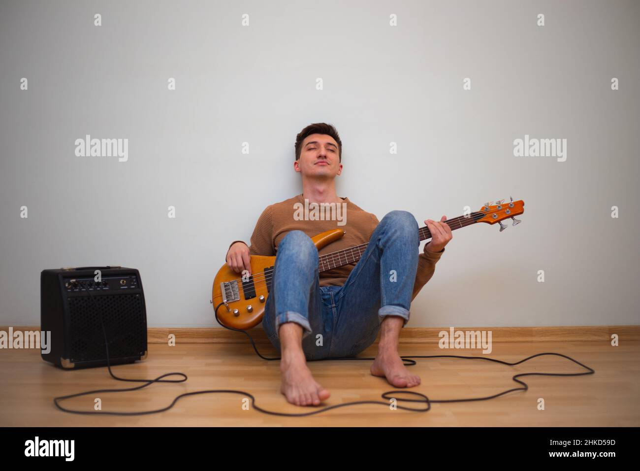 Junger Mann spielt auf einer Gitarre mit einer Wand im Hintergrund Stockfoto