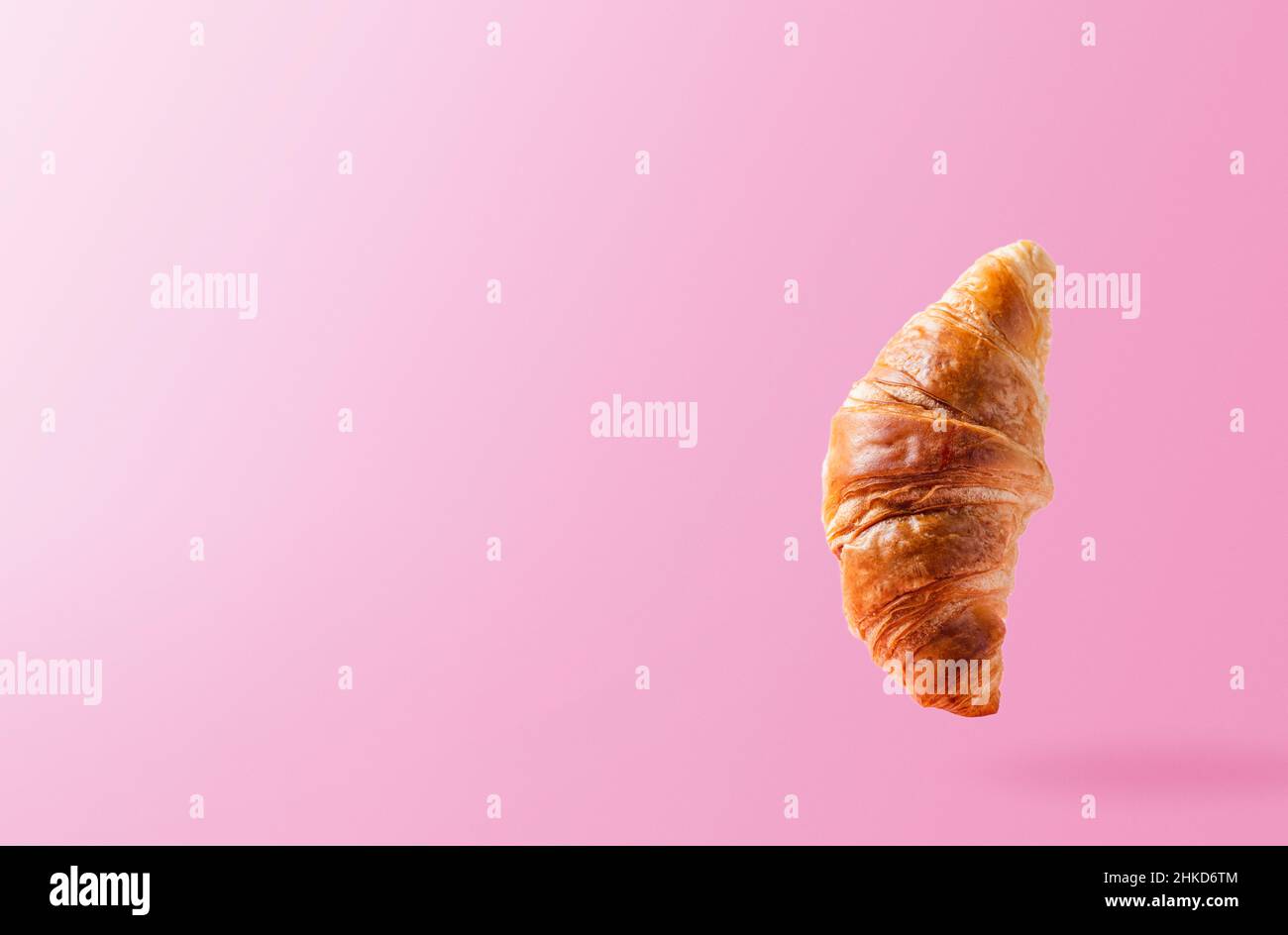 Frisch gebackene Croissants schweben oder fliegen. Croissant fliegen in der Luft isoliert auf rosa Hintergrund. Levitation-Szene. Platz kopieren. Schildermockup oder Werbung für Bäckerei, Süßwaren Stockfoto