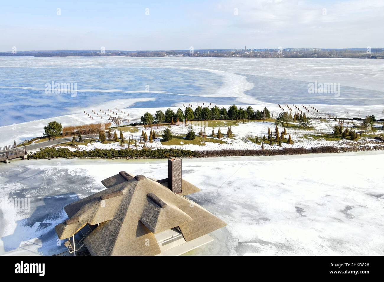 Winter wunderschöne Landschaft mit einem gefrorenen Fluss und kleinen Häusern mit Schilfdächern auf der Insel. Rustikaler Stil, Strohdach, Satteldach. Luftaufnahme Drohne vi Stockfoto