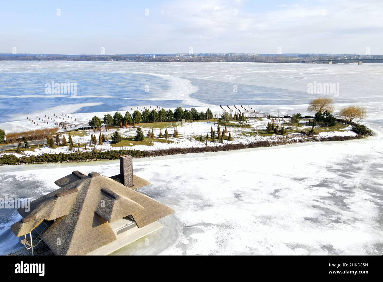 Winter wunderschöne Landschaft mit einem gefrorenen Fluss und kleinen Häusern mit Schilfdächern auf der Insel. Rustikaler Stil, Strohdach, Satteldach. Luftaufnahme Drohne vi Stockfoto