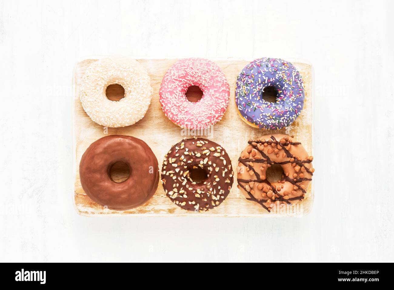 Sechs farbenfrohe glasierte süße Donuts auf einem weißen Holzbrett. Draufsicht, Platz für Text kopieren Stockfoto