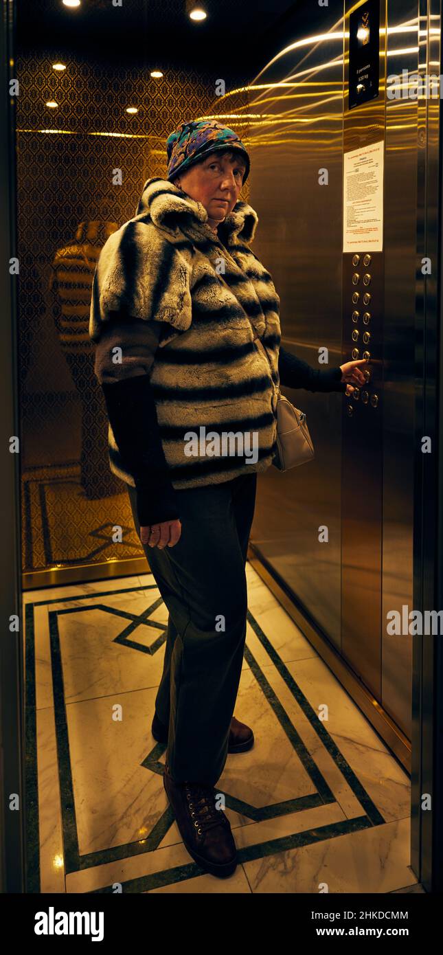 Vertikales Foto einer ziemlich reifen erwachsenen Frau, die in einem Hochhaus in einem Aufzug einen Knopf drückt. Stockfoto