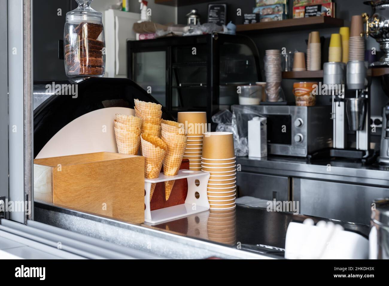 Viele leere gebackene Waffelkonen und Pappbecher für Eis, die am Schaufenster des Straßencafés zum Mitnehmen gestapelt wurden. Süße Desserts und Stockfoto