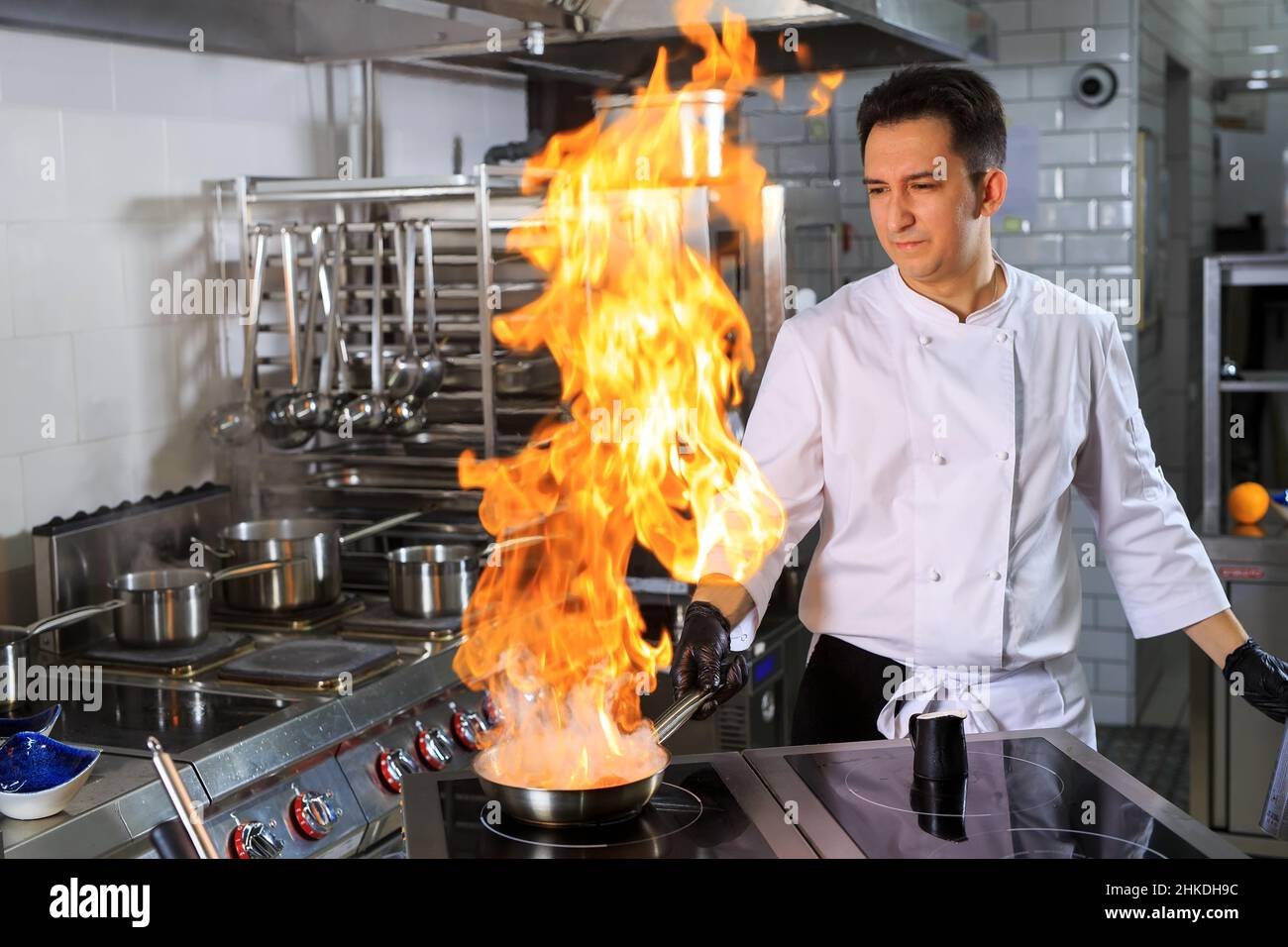 Nahaufnahme der Hände des Küchenchefs, die Speisen auf Feuer kochen. Der Koch verbrennt Essen in einer professionellen Küche Stockfoto
